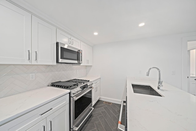 kitchen with appliances with stainless steel finishes, a sink, backsplash, white cabinets, and light stone counters