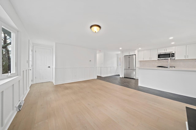 unfurnished living room featuring a wainscoted wall, wood finished floors, recessed lighting, and a decorative wall