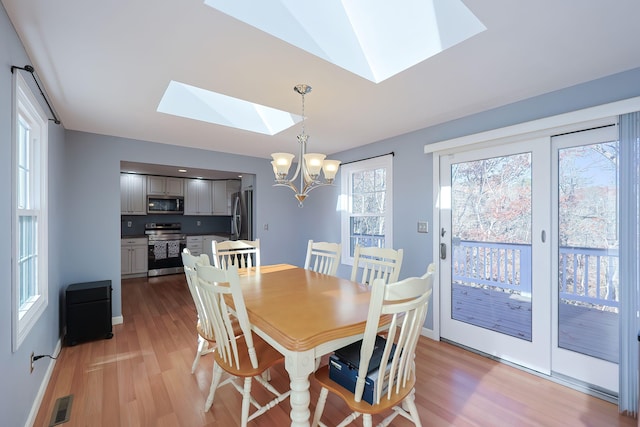 dining room with light hardwood / wood-style floors, lofted ceiling with skylight, and a chandelier