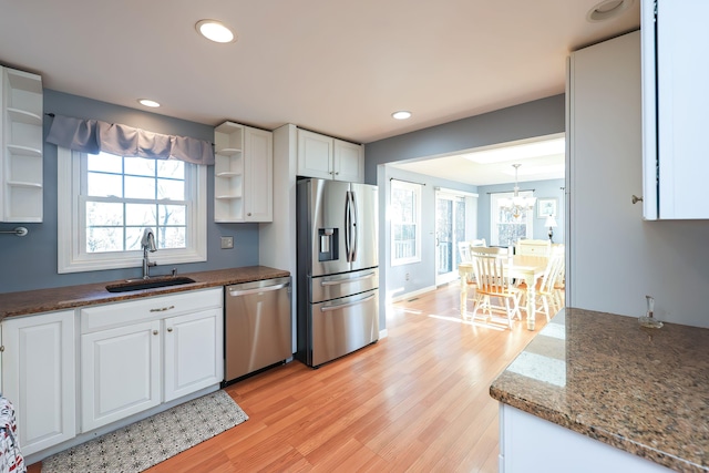 kitchen with appliances with stainless steel finishes, white cabinetry, dark stone counters, light hardwood / wood-style floors, and sink