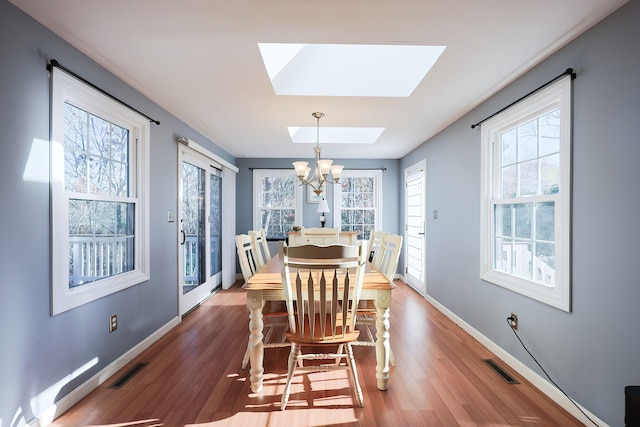 dining space featuring hardwood / wood-style flooring, a skylight, and an inviting chandelier