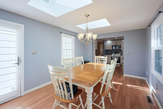 dining room with a skylight, a chandelier, a healthy amount of sunlight, and light hardwood / wood-style flooring