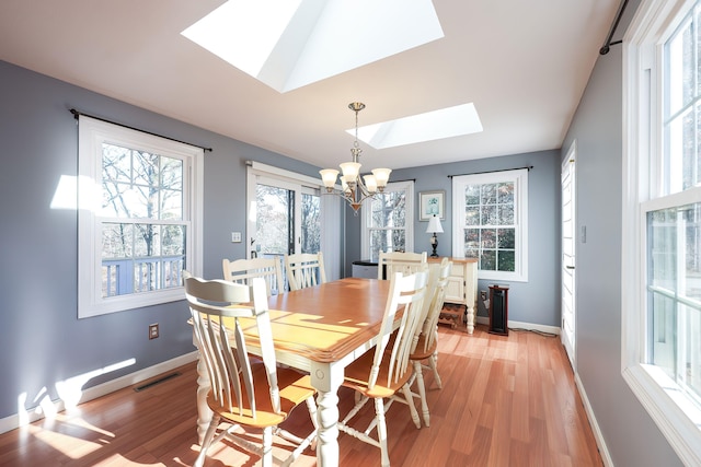 dining space with light wood-type flooring, a notable chandelier, and a skylight