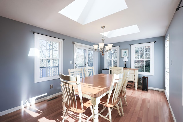 dining room with light hardwood / wood-style flooring, a skylight, and an inviting chandelier