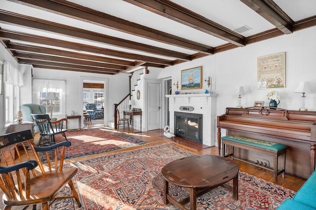 living room featuring a fireplace, wood finished floors, visible vents, stairs, and beamed ceiling