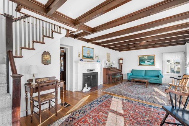 living area featuring stairs, beamed ceiling, a fireplace, and wood finished floors