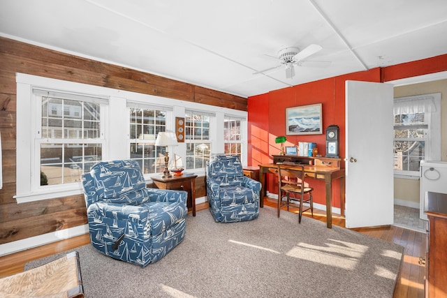 living area featuring ceiling fan, baseboards, hardwood / wood-style flooring, and wooden walls