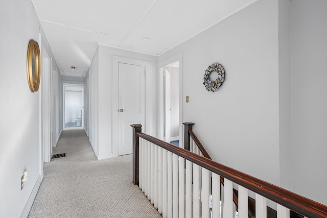 hallway with attic access, visible vents, light colored carpet, and an upstairs landing