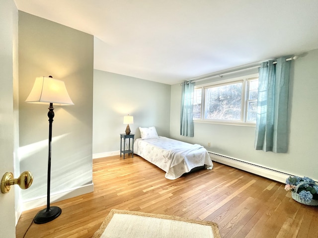 bedroom with a baseboard radiator, baseboards, and light wood-style flooring