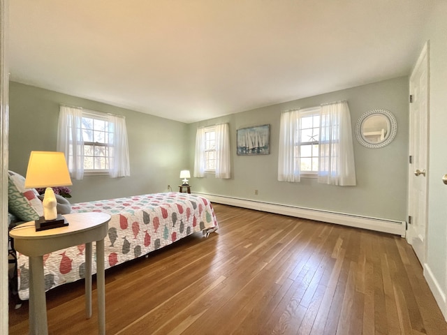 bedroom featuring multiple windows, a baseboard heating unit, and hardwood / wood-style flooring