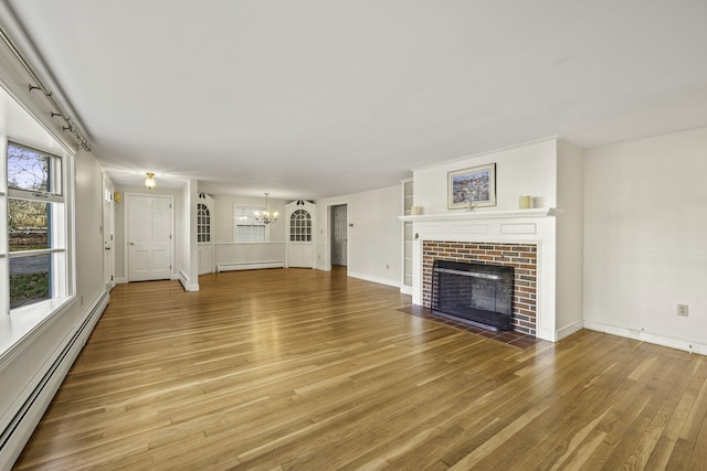 unfurnished living room featuring a baseboard heating unit, a tiled fireplace, a notable chandelier, and light wood finished floors