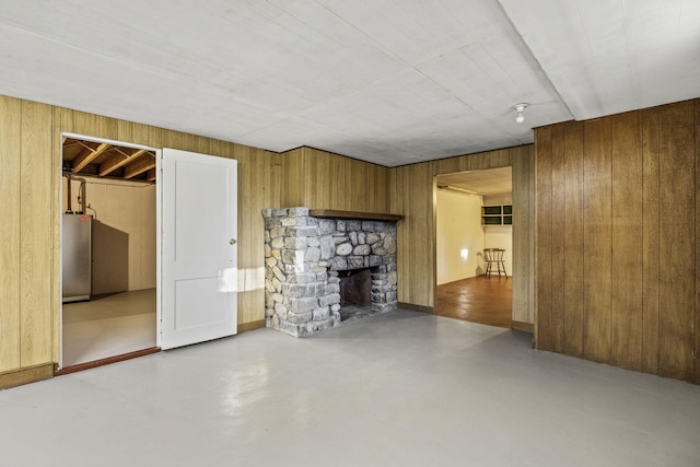 unfurnished living room featuring concrete flooring, a stone fireplace, and wood walls