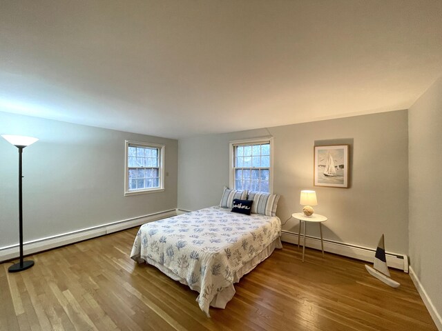 bedroom featuring a baseboard heating unit, multiple windows, and wood finished floors