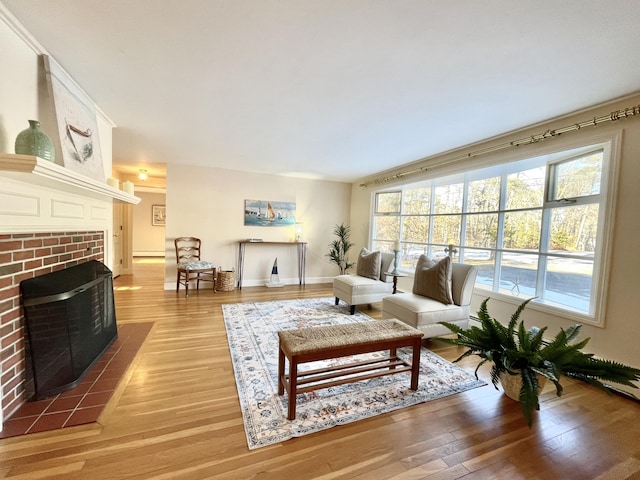 living room with light wood-style flooring, a brick fireplace, and baseboards