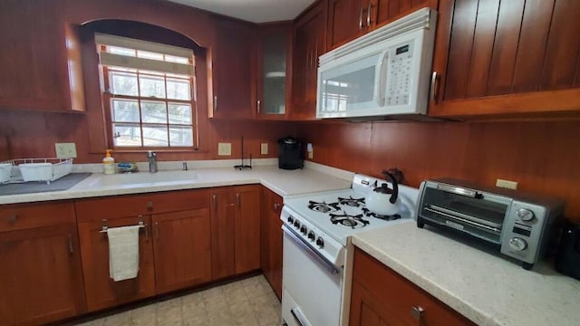 kitchen with glass insert cabinets, white appliances, a sink, brown cabinets, and light countertops