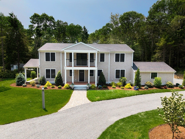 73 Tern Ln, Centerville, MA 02632 - greek revival house with a balcony, covered porch, a front yard, and view of scattered trees