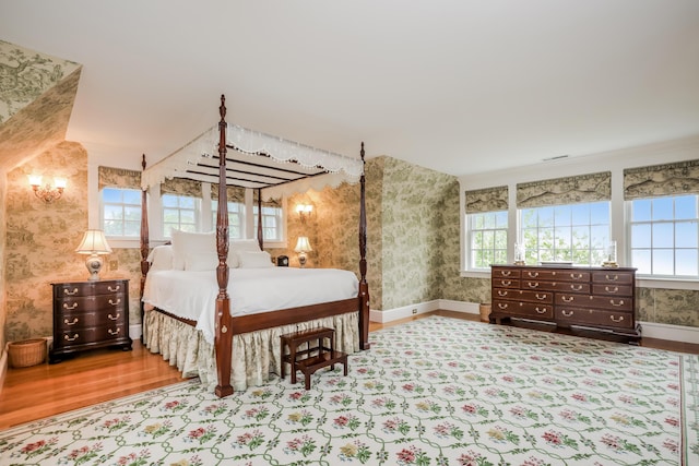 bedroom featuring multiple windows, wallpapered walls, wood finished floors, and baseboards