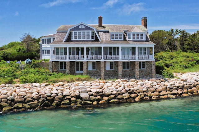 back of house with a chimney, a balcony, and stone siding