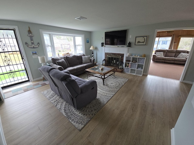 living area featuring visible vents, a glass covered fireplace, a healthy amount of sunlight, and wood finished floors