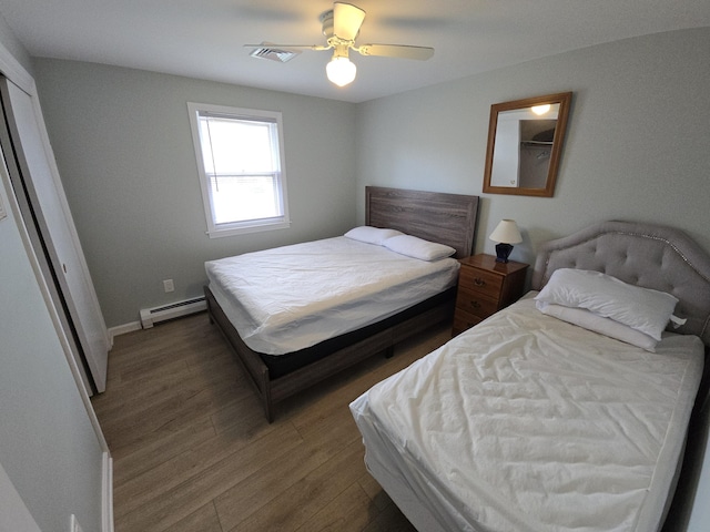 bedroom featuring visible vents, a ceiling fan, baseboards, wood finished floors, and a baseboard heating unit