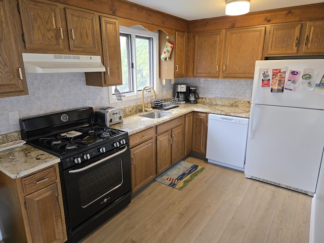 kitchen featuring a sink, under cabinet range hood, brown cabinets, and white appliances
