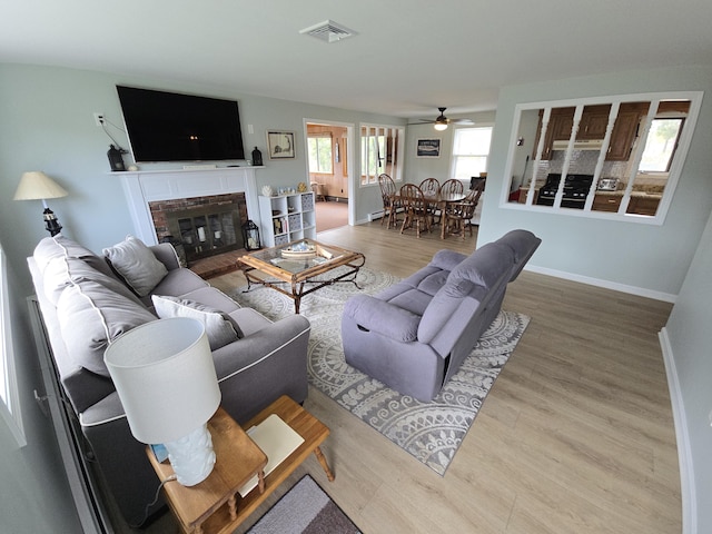 living room with ceiling fan, a fireplace, baseboards, wood finished floors, and visible vents