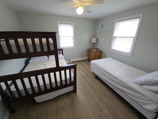 bedroom featuring ceiling fan, visible vents, baseboard heating, wood finished floors, and baseboards