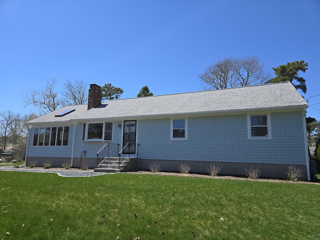 ranch-style house with roof with shingles, a front yard, and a chimney