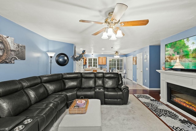 living area with ceiling fan, light wood-type flooring, a glass covered fireplace, and baseboards