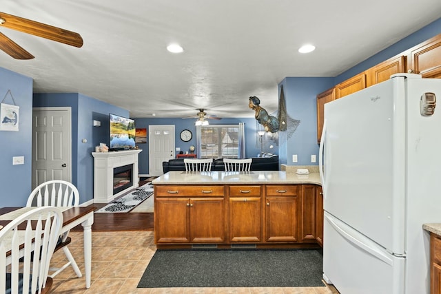 kitchen with brown cabinetry, a glass covered fireplace, open floor plan, freestanding refrigerator, and light tile patterned flooring