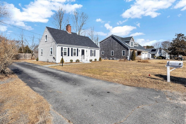 view of front of house with aphalt driveway, a chimney, a shingled roof, and a front lawn