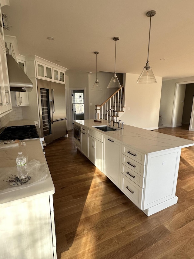 kitchen with sink, hanging light fixtures, built in appliances, white cabinets, and a kitchen island