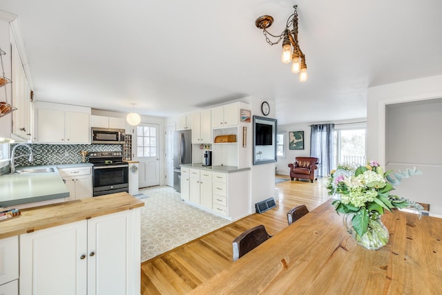 kitchen featuring a sink, butcher block countertops, appliances with stainless steel finishes, open floor plan, and white cabinets
