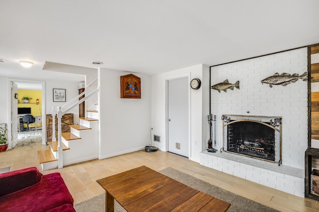 living room featuring stairs, visible vents, wood finished floors, and a brick fireplace