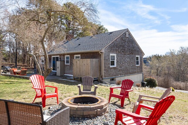 back of house with a lawn, an outdoor fire pit, and roof with shingles