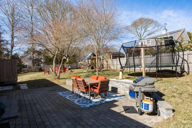 view of patio with a trampoline, a grill, a fenced backyard, outdoor dining area, and a playground