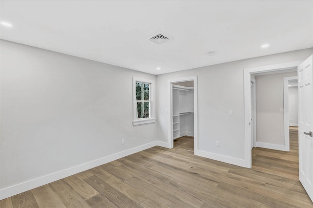 unfurnished bedroom featuring a walk in closet, a closet, and light hardwood / wood-style flooring