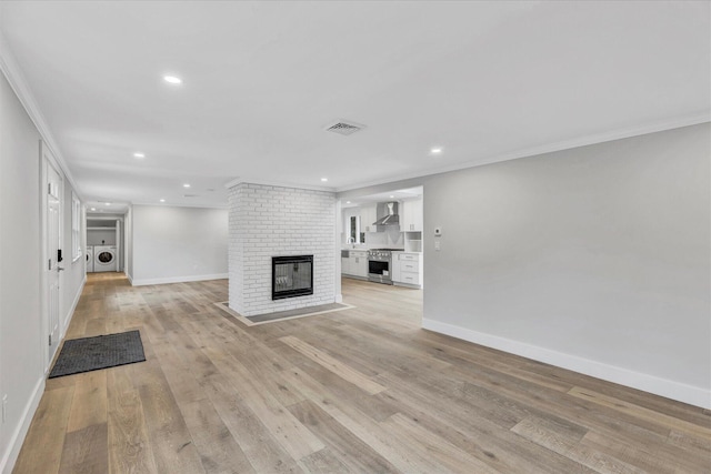 unfurnished living room featuring crown molding, a brick fireplace, separate washer and dryer, and light hardwood / wood-style floors