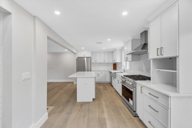 kitchen with wall chimney range hood, sink, white cabinetry, stainless steel appliances, and a kitchen island