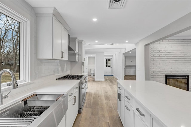 kitchen with white cabinets, sink, stainless steel stove, and light wood-type flooring