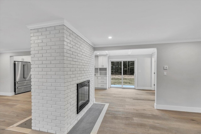 unfurnished living room featuring a brick fireplace, crown molding, and light wood-type flooring