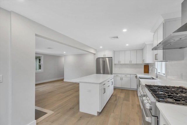 kitchen featuring sink, white cabinets, premium appliances, a center island, and wall chimney exhaust hood