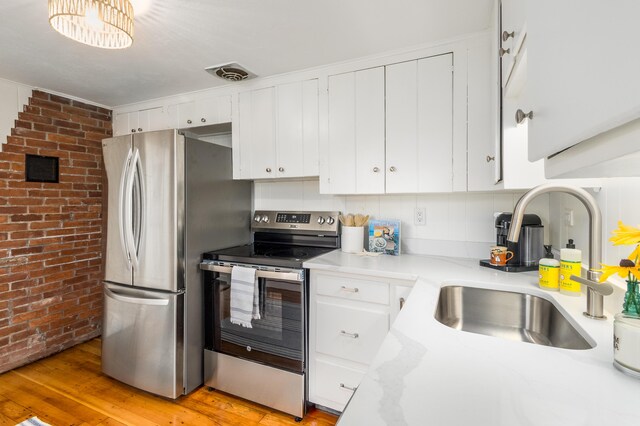 429 Paines Creek Rd, Brewster, MA 02631 - kitchen featuring appliances with stainless steel finishes, brick wall, light countertops, light wood-style flooring, and white cabinetry