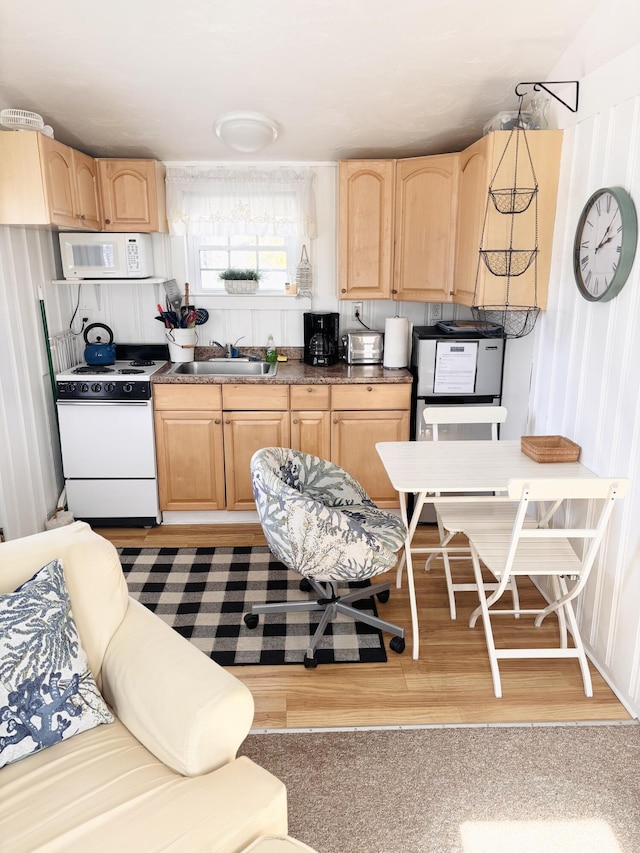 kitchen with light brown cabinetry, dark countertops, white appliances, and a sink