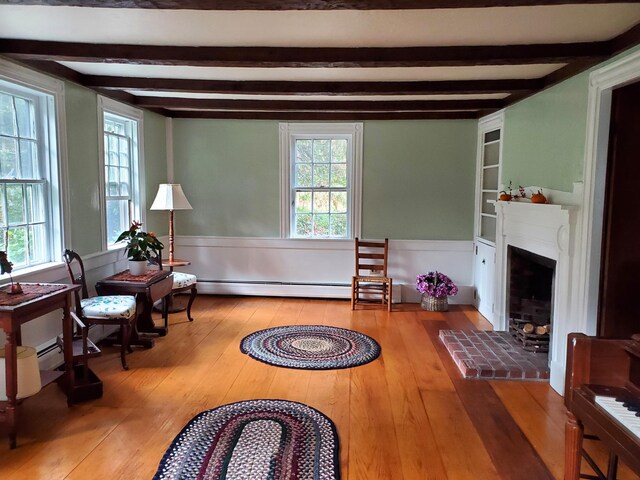 living area with built in shelves, a brick fireplace, baseboard heating, plenty of natural light, and hardwood / wood-style floors