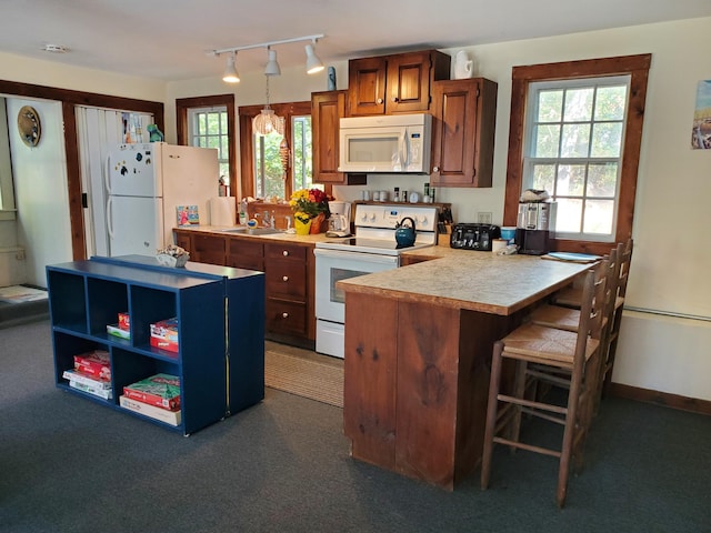 kitchen featuring pendant lighting, sink, white appliances, rail lighting, and a kitchen breakfast bar