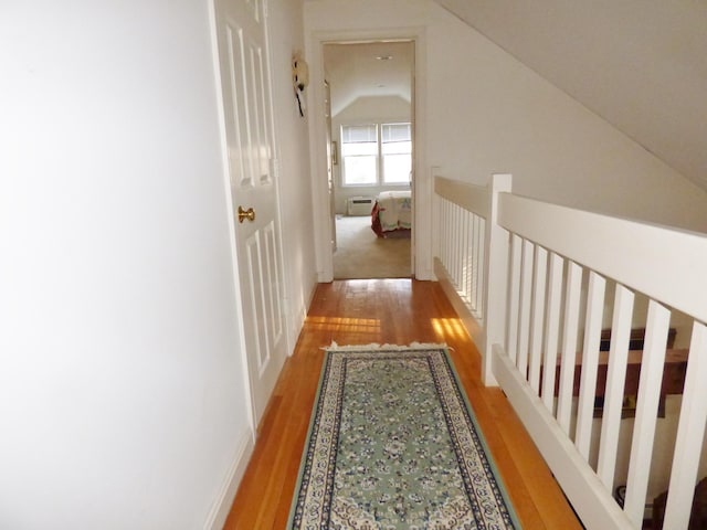 hallway with a wall unit AC, lofted ceiling, and light hardwood / wood-style flooring