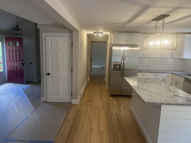 kitchen with stainless steel fridge, hanging light fixtures, white cabinets, light stone counters, and decorative backsplash