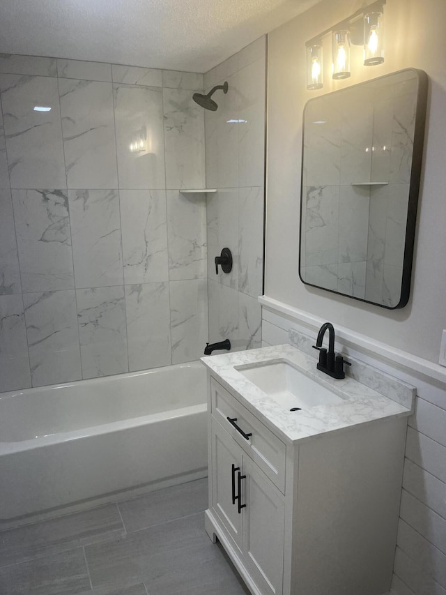 bathroom featuring a textured ceiling, tiled shower / bath combo, and vanity