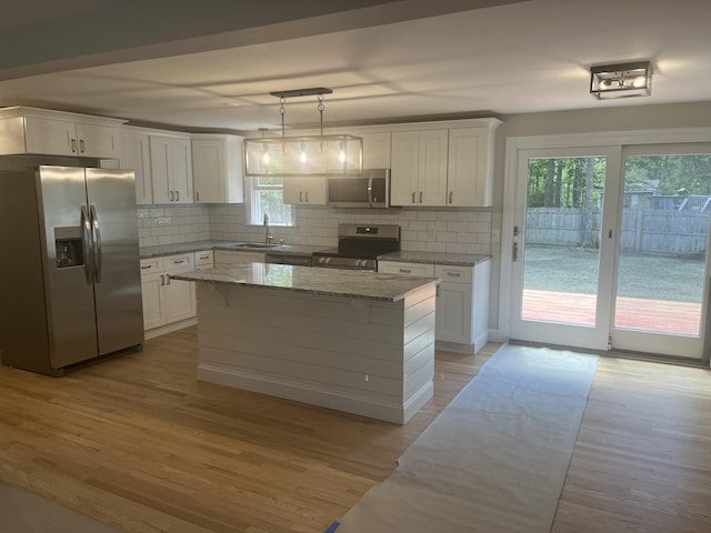 kitchen featuring appliances with stainless steel finishes, a kitchen island, white cabinetry, backsplash, and hanging light fixtures